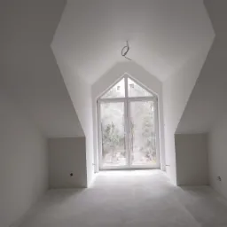 Poddasze po malowaniu na biało z oknem szczytowym i wystającymi przewodami elektrycznymi, widok na zewnątrz przez okno.
