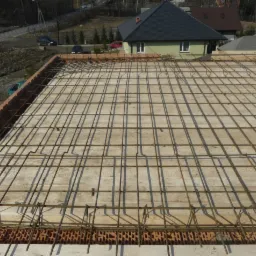 Zbrojenie stropu na deskowaniu z ceglanym obramowaniem w Bielsko-Białej, widok z góry na budowę z domami w tle.