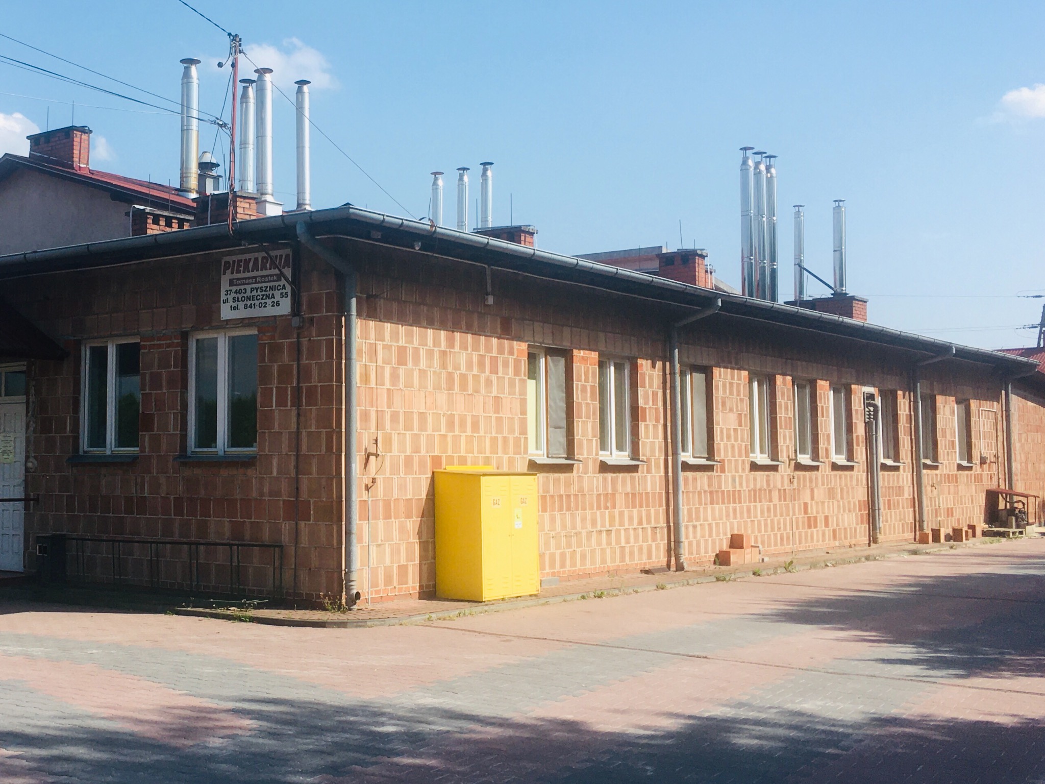 Budynek piekarni z cegły z wieloma kominami ze stali nierdzewnej na dachu, żółta szafka gazowa przy ścianie
