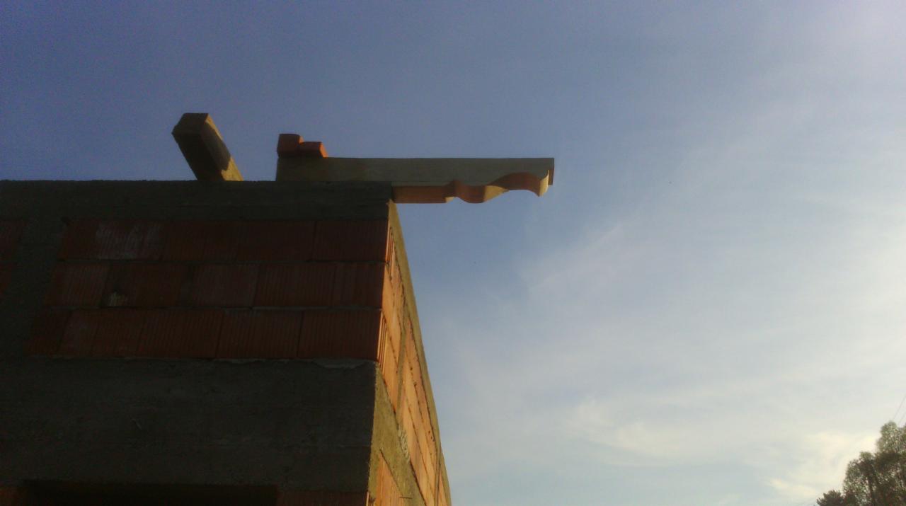 Wznoszenie muru z pustaków ceramicznych z elementami więźby dachowej pod błękitnym niebem. Widok z dołu na surowy stan budynku.