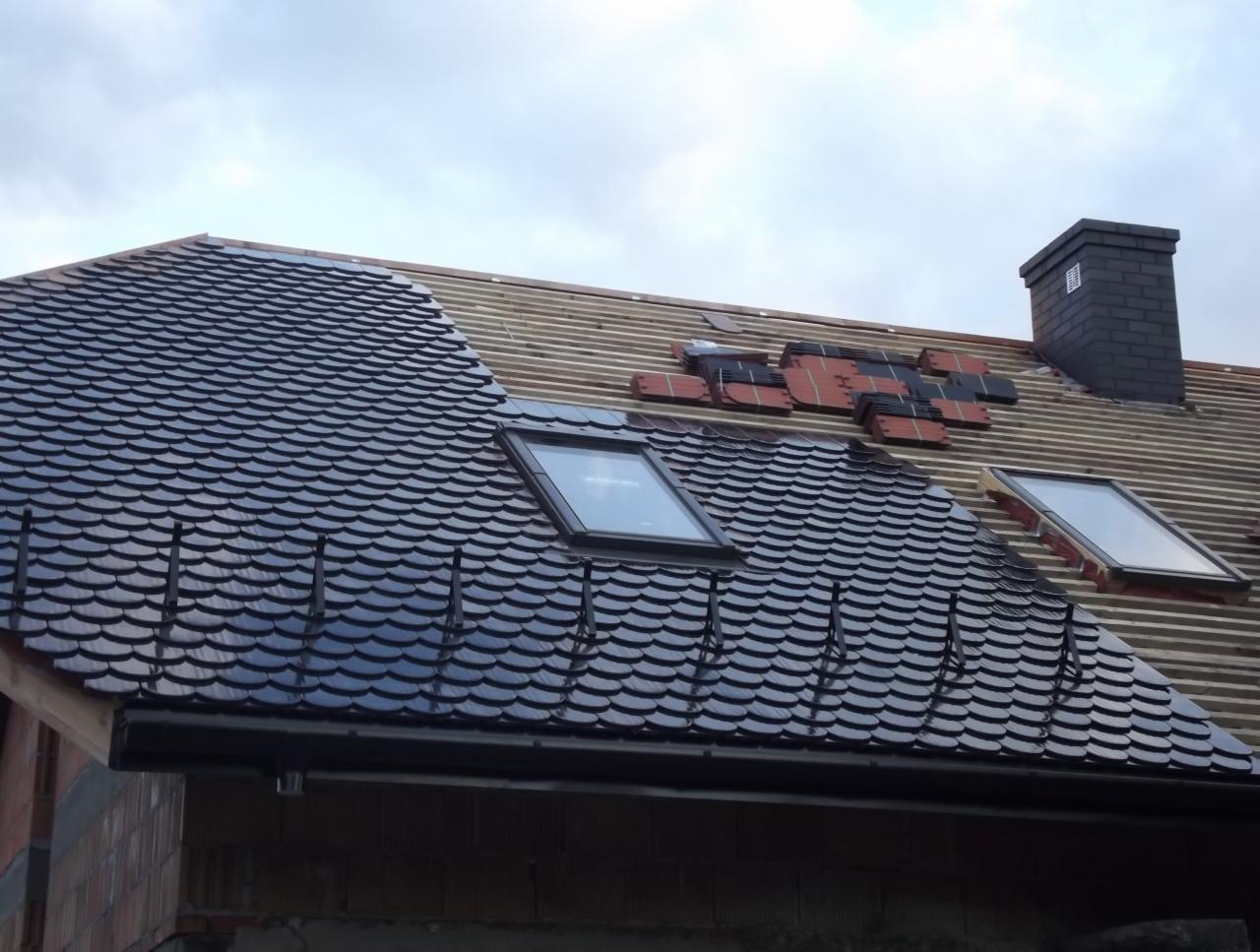 Układanie dachówki karpiówki na dachu z oknami połaciowymi w Skawie. Część dachu pokryta, część w trakcie prac. Widoczny komin i elementy konstrukcji.