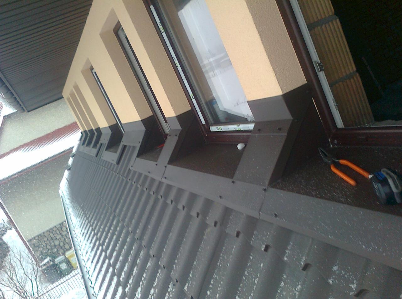 Szary dach z blachy trapezowej z oknami dachowymi i narzędziami. Widok z dołu na budynek w trakcie opadów śniegu.