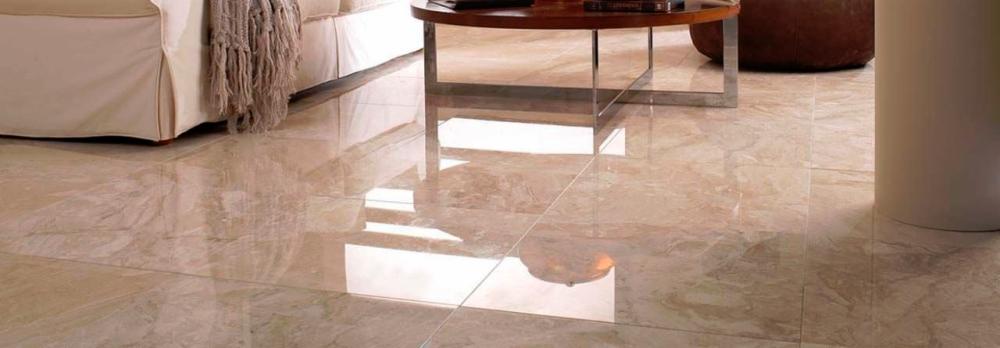 Błyszcząca podłoga z marmurowych płytek w odcieniach beżu i brązu, odbijająca światło, z fragmentami mebli w tle.