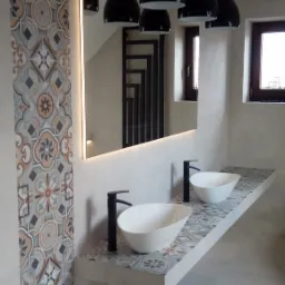 Nowoczesna łazienka z podwójną umywalką nablatową, czarną armaturą i lustrem z podświetleniem LED, wykończona płytkami w stylu patchwork na ścianie i blacie.