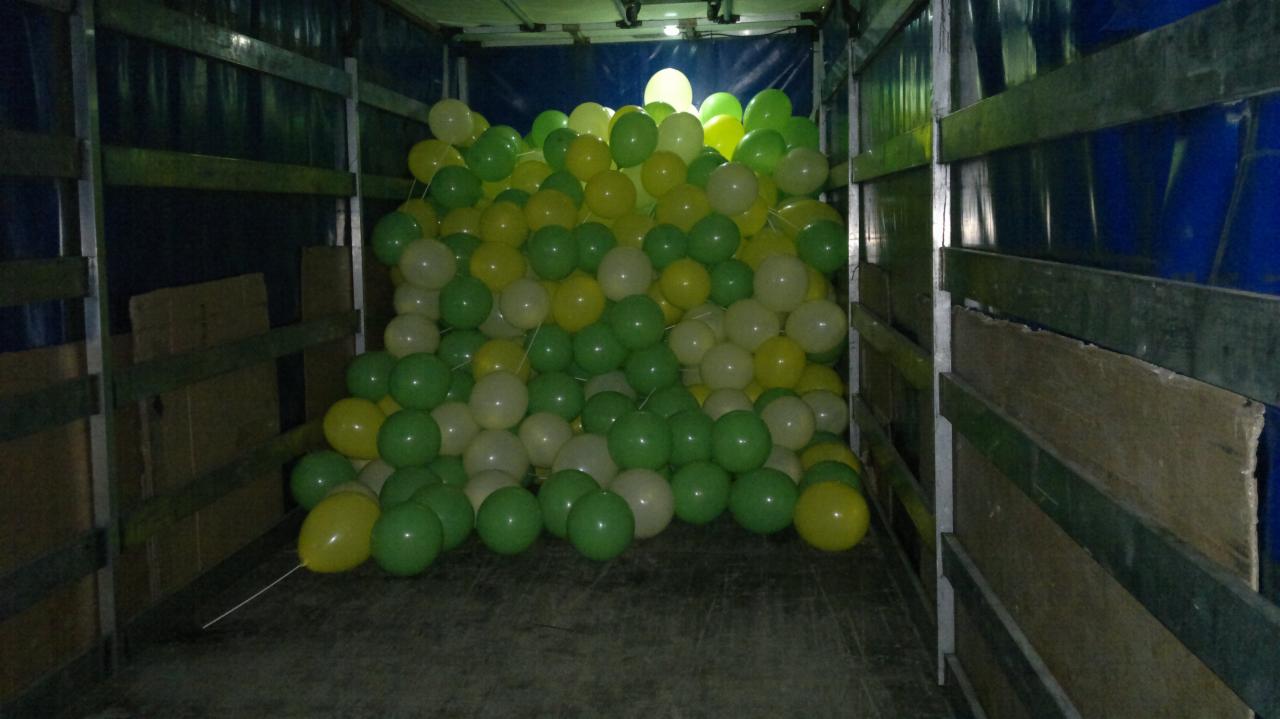 Wnętrze ciężarówki wypełnione zielonymi, żółtymi i białymi balonami. Balony szczelnie wypełniają przestrzeń ładunkową, widoczne ściany i podłoga pojazdu.