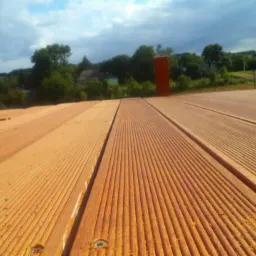 Deski tarasowe z widocznymi śrubami montażowymi i fragmentem krajobrazu w tle, ujęcie z niskiej perspektywy. Drewno o ciepłej barwie.