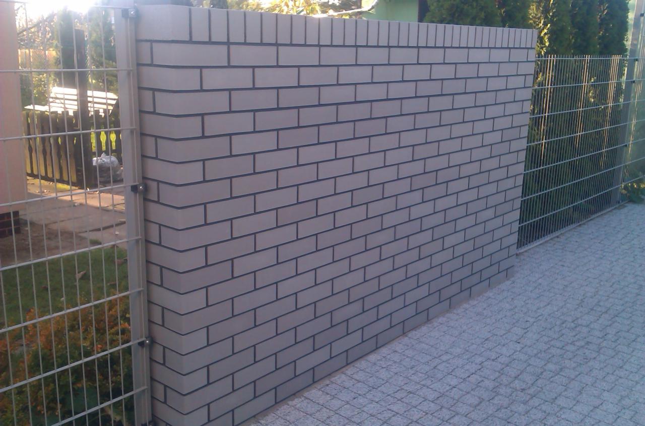 Nowoczesne ogrodzenie z szarej cegły i metalowej siatki, widok z bliska na połączenie materiałów i fakturę brukowanej nawierzchni.