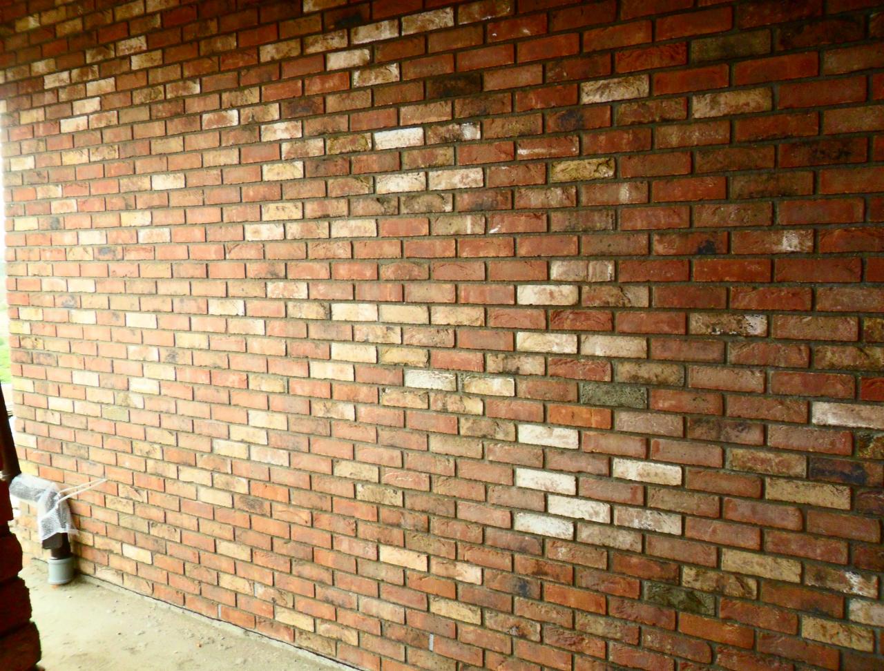 Mur z czerwonej cegły z elementami białej i żółtej, ułożony pod kątem, widoczne spoiny i fragment konstrukcji z lewej strony. Tekstura cegieł z bliska.