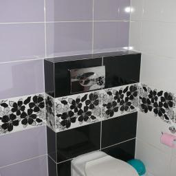 LUKSUS Styl  ŁUKASZ KORNILAK - Wykończona łazienka: podwieszana toaleta z czarno-białą obudową w kwiaty, fioletowe i białe płytki na ścianach, wentylator w górnym rogu.