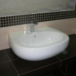 LUKSUS Styl  ŁUKASZ KORNILAK - Nowoczesna, biała umywalka z chromowaną baterią na tle mozaiki i beżowych płytek w łazience. Widoczne ciemne płytki podłogowe.