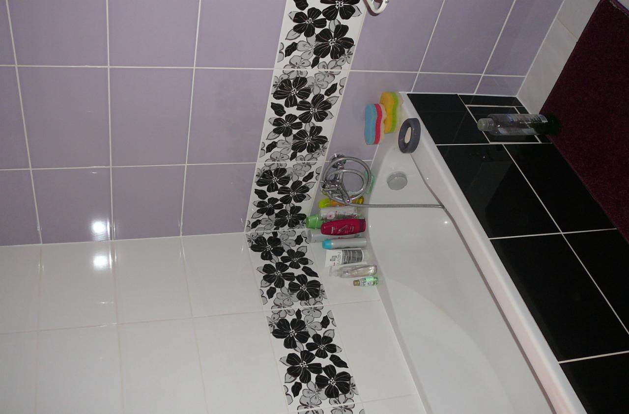 Wykończona łazienka z wanną, czarno-białym motywem kwiatowym na płytkach i fioletowymi akcentami. Widoczne kosmetyki i akcesoria kąpielowe.