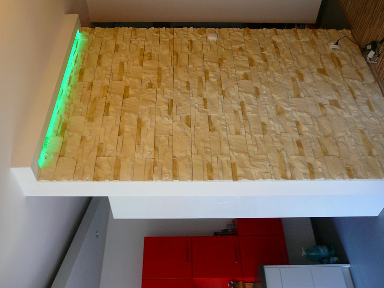 Ściana z dekoracyjnej cegły z podświetleniem LED w Sokołowie Podlaskim. Beżowa okładzina, biały sufit podwieszany, fragment czerwonej zabudowy kuchennej w tle.