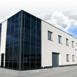 Nowoczesny budynek biurowy z dużą szklaną fasadą i tynkowaną elewacją, widoczne silosy przemysłowe w tle.