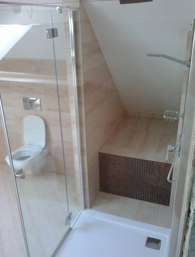 Wykończona łazienka na poddaszu: kabina prysznicowa ze szklanymi drzwiami, beżowe płytki, mozaika i toaleta pod skosem dachu. Minimalistyczny design.