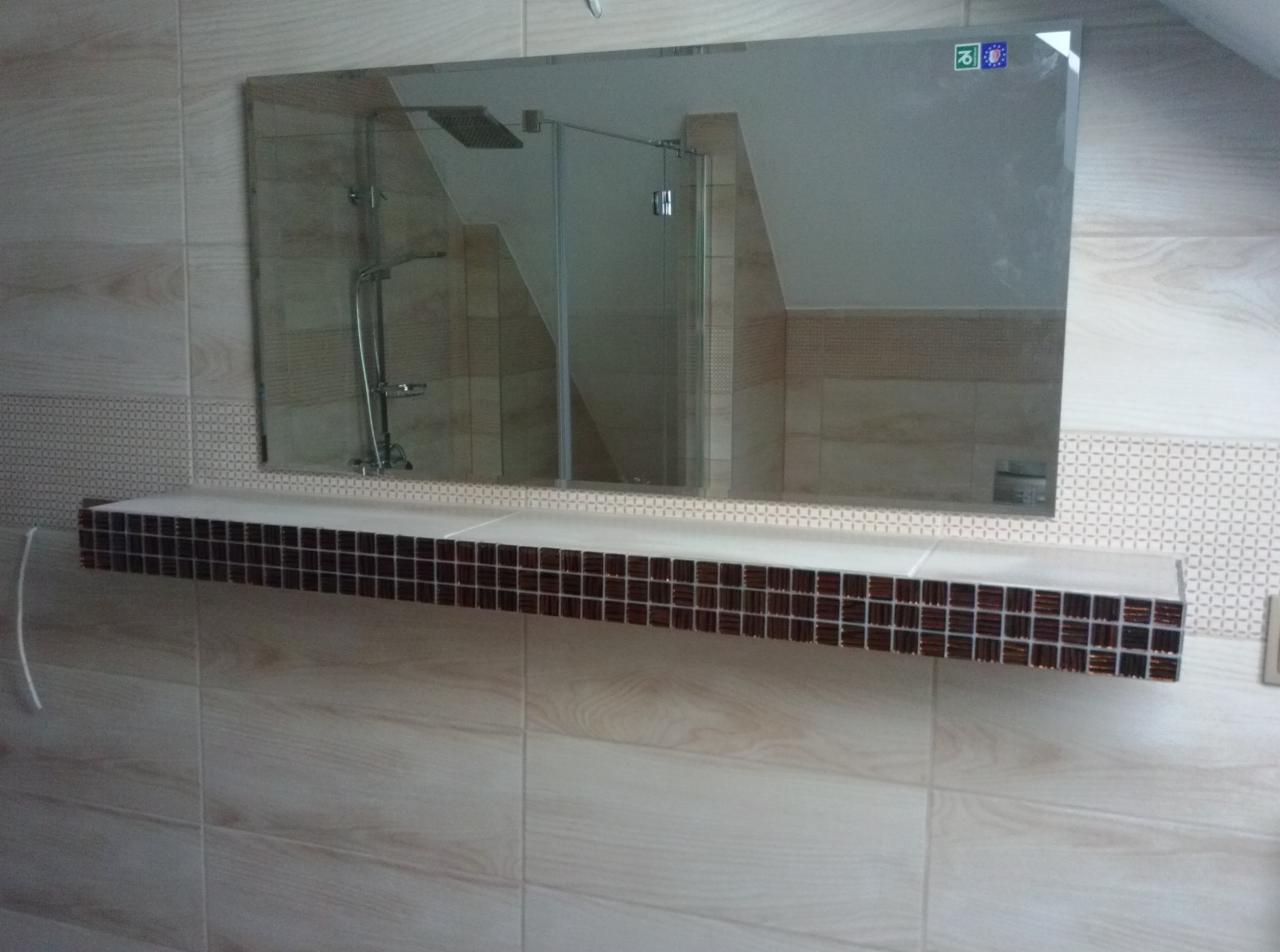 Wykończona łazienka w Bytomiu: lustro nad półką z mozaiki, jasne płytki imitujące drewno, widoczna kabina prysznicowa. Estetyczne i funkcjonalne rozwiązanie.