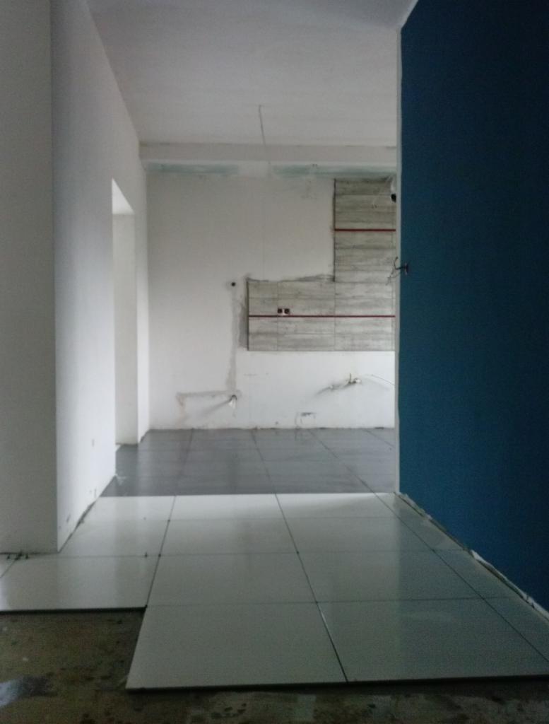 Wnętrze w trakcie remontu: białe płytki podłogowe częściowo ułożone, ściany przygotowane do malowania. Fragment niebieskiej ściany po prawej.