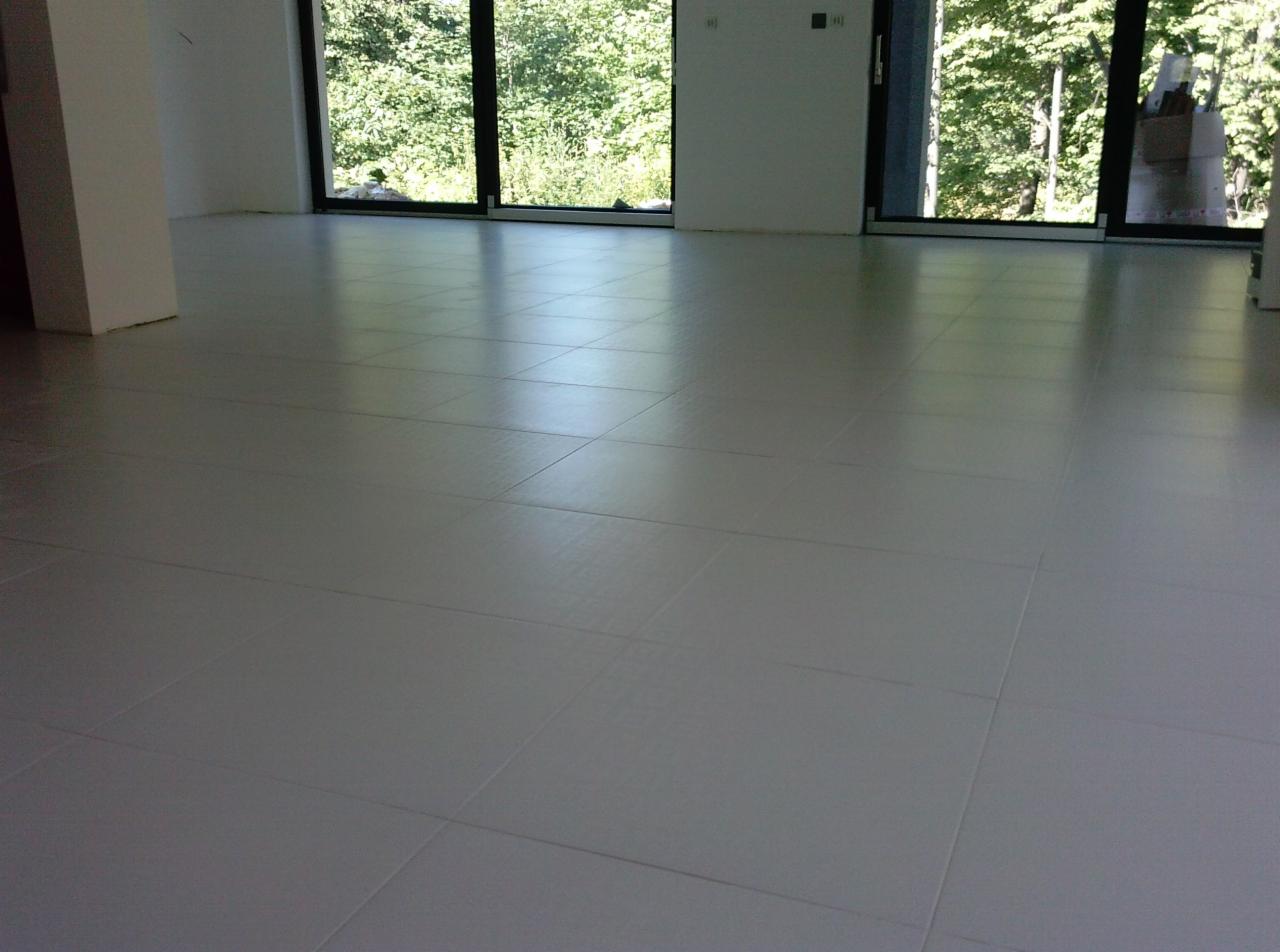 Jasne, połyskujące płytki podłogowe ułożone w nowym wnętrzu z dużymi oknami i widokiem na zieleń, podkreślone subtelnym oświetleniem.