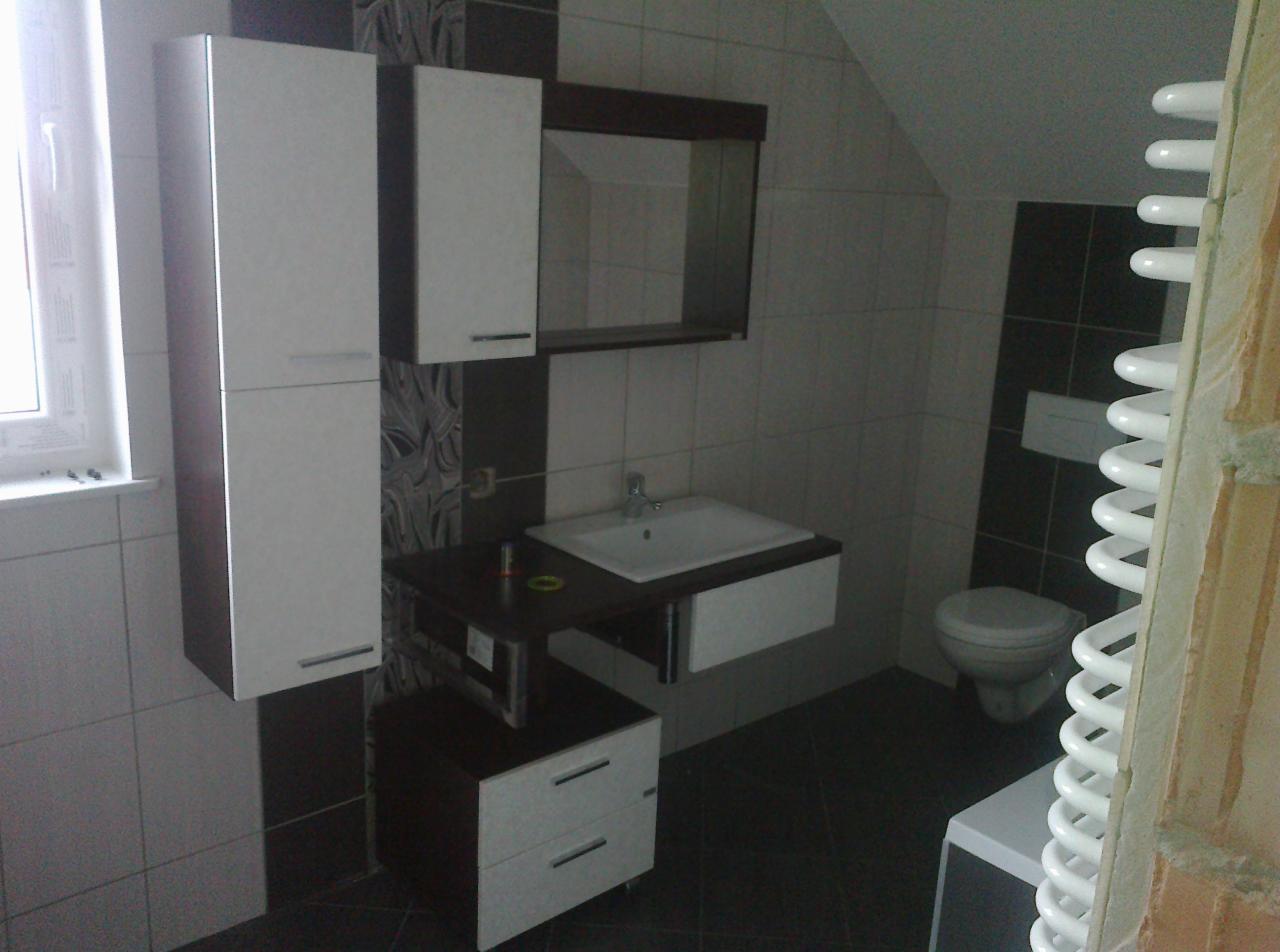 Wykończona łazienka w odcieniach bieli i brązu, z wiszącymi szafkami, umywalką z szafką i grzejnikiem drabinkowym. Widoczne płytki na ścianach i podłodze.