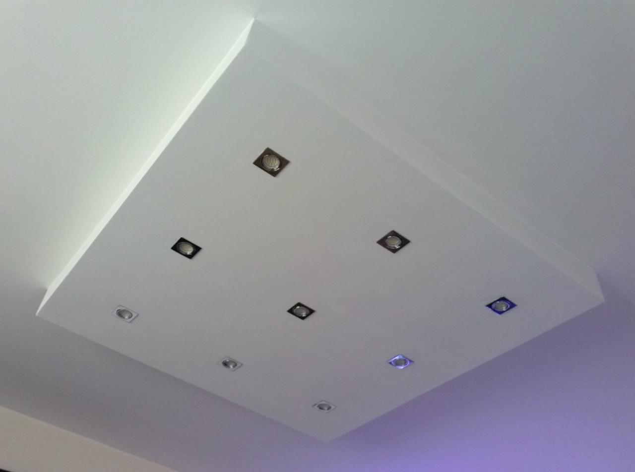 Podwieszany sufit z punktowym oświetleniem LED o różnej barwie, wkomponowany w białą płaszczyznę sufitu, z widocznym fragmentem ściany w tle.