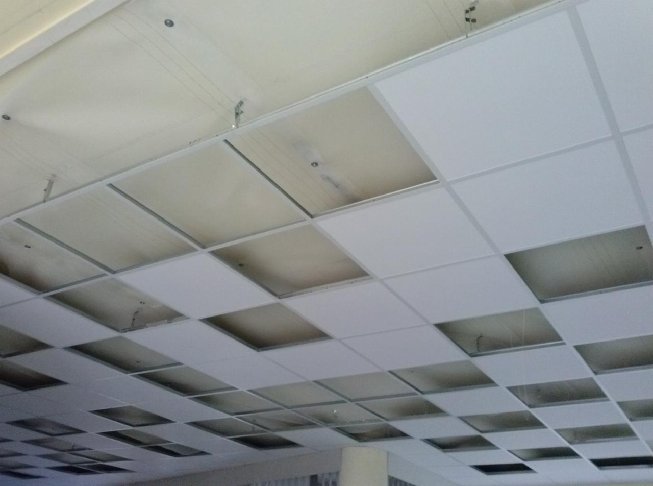 Sufit podwieszany kasetonowy w trakcie montażu, widoczne elementy konstrukcyjne i częściowo zamontowane białe płyty. Ujęcie z dołu, perspektywa zbieżna.