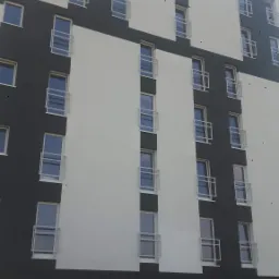 Wielopiętrowy budynek z elewacją w kolorach biało-grafitowych, widoczne puszki z farbą i folia malarska na dole, elewacja z balkonami.