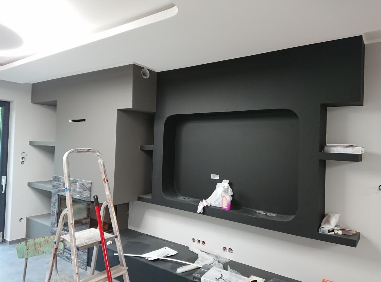 Szara ściana z wnęką pomalowaną na czarno, widoczne półki, drabina malarska i akcesoria malarskie, sufit pomalowany na biało.
