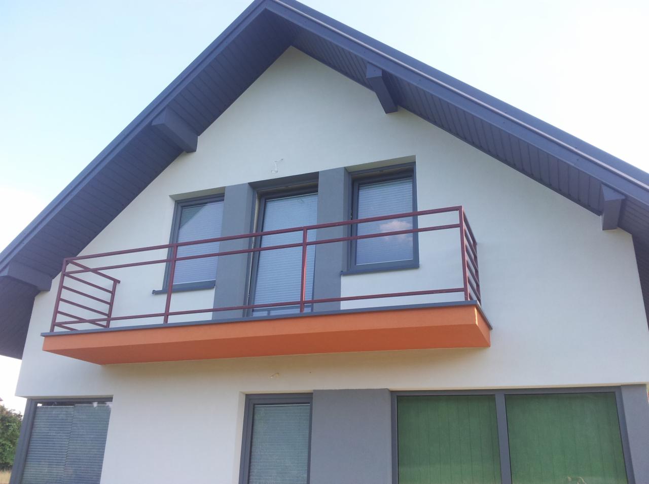 Elewacja domu jednorodzinnego z balkonem, wykończona w jasnych kolorach z grafitowymi detalami dachu i okien. Balkon z pomarańczową podłogą i bordową barierką.