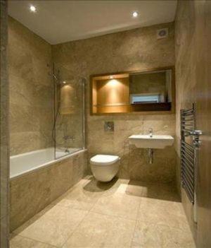 Beżowa łazienka z kabiną prysznicową, toaletą, umywalką i grzejnikiem drabinkowym. Oświetlenie punktowe sufitowe. Ujęcie z perspektywy wejścia.