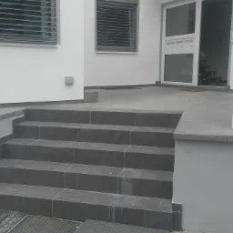 Wykończone schody wejściowe do domu, wyłożone ciemnoszarą płytką, z widocznymi detalami wykończenia i fragmentem elewacji budynku.