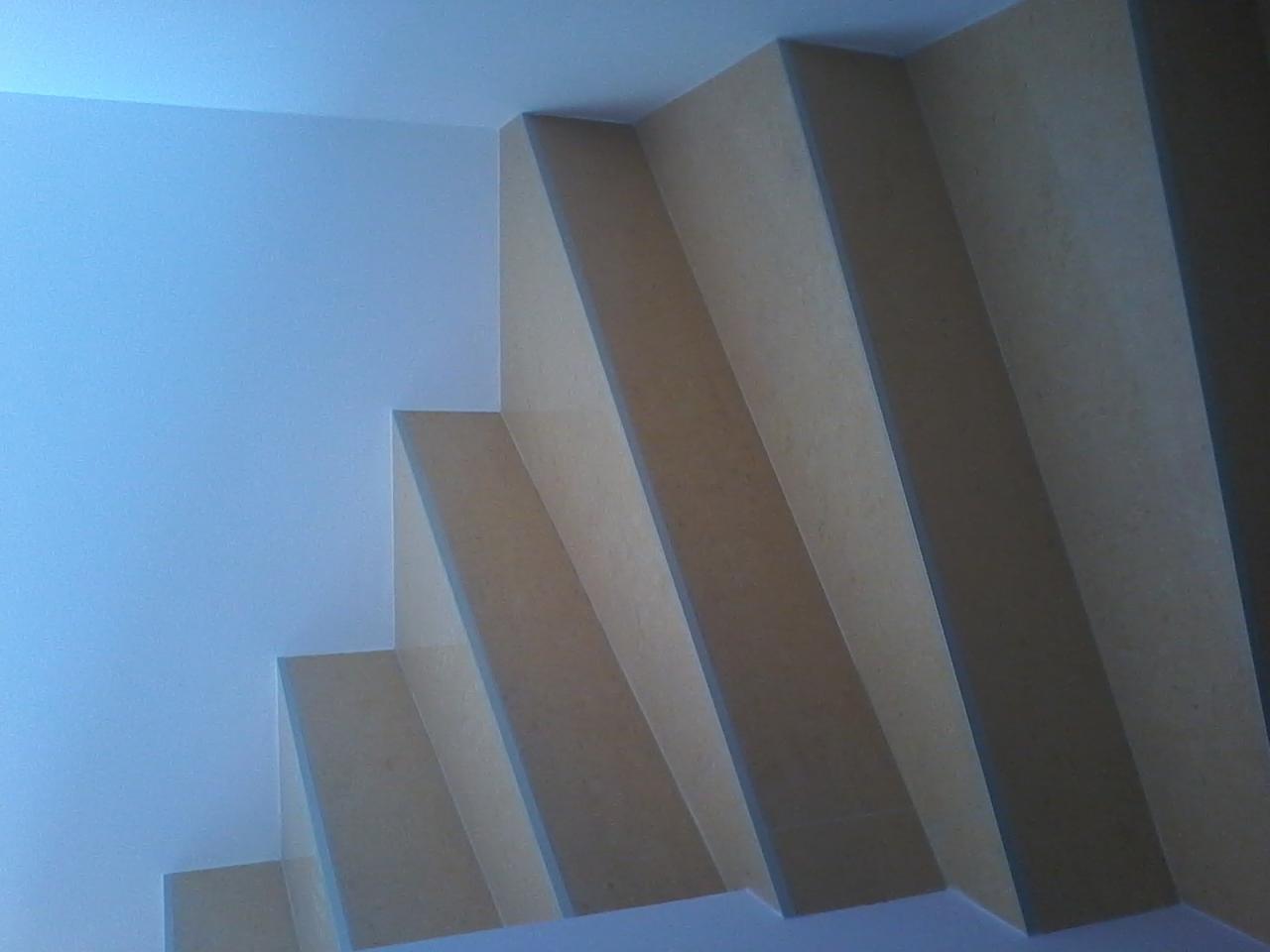 Nowoczesna, surowa konstrukcja z płyt MDF na balkonie, widoczna z dołu pod kątem. Minimalistyczny design z jasną ścianą w tle, światło naturalne.