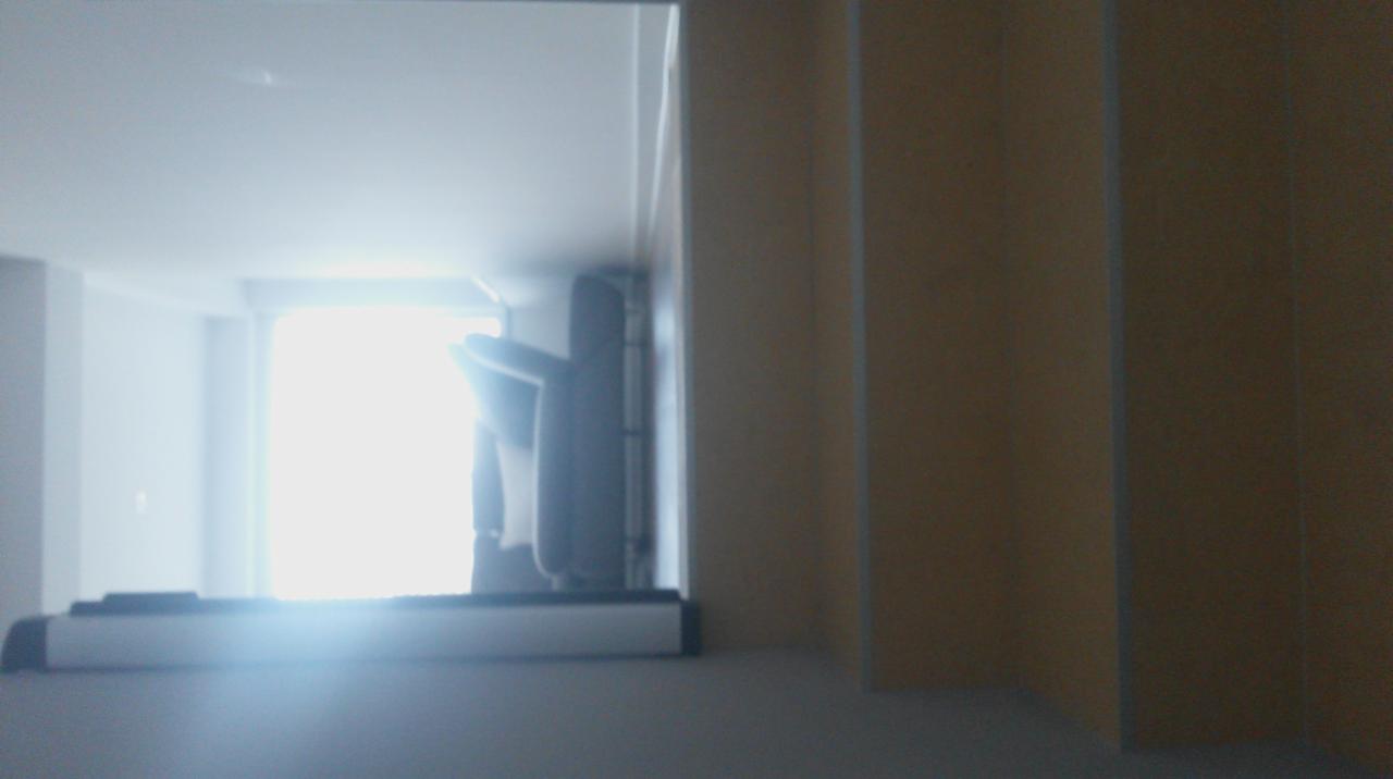 Jasne wnętrze z widokiem na balkon przez otwór w ścianie. Widoczne fragmenty zabudowy balkonu i ściany w odcieniach beżu.