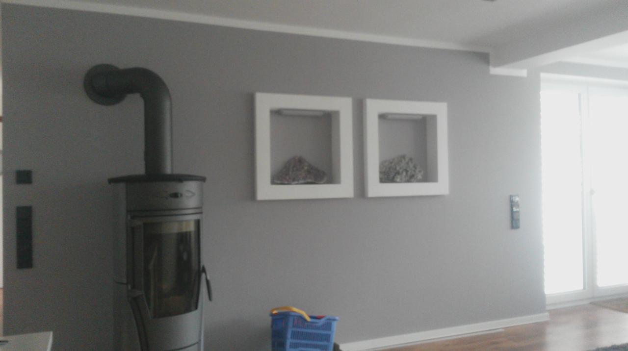 Szare wnętrze z kominkiem typu koza i dwoma podświetlanymi, kwadratowymi wnękami dekoracyjnymi na ścianie. Widoczne panele podłogowe i niebieski koszyk.