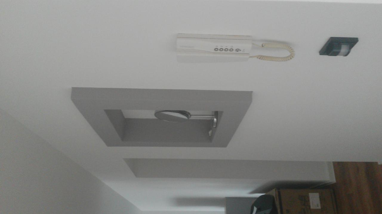 Szary sufit podwieszany z oświetleniem punktowym i panelem domofonu. Widok z dołu.