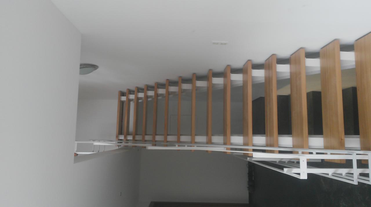 Nowoczesna balustrada balkonowa z drewnianymi panelami i białymi metalowymi elementami konstrukcyjnymi, widziana z dołu pod kątem. Minimalistyczny design.