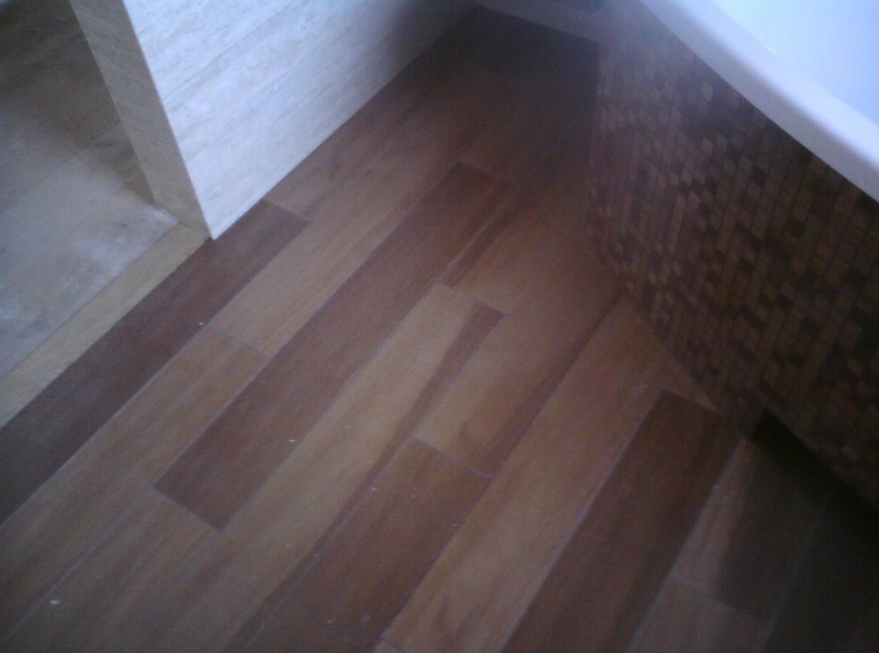 Ukończona łazienka: parkiet drewnopodobny na podłodze, mozaika na ścianie przy wannie. Detal wykończenia, ciepłe barwy.