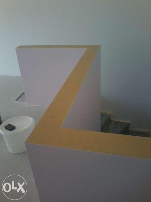 Konstrukcja z płyt karton-gips na balkonie w trakcie prac, widoczna puszka z farbą i fragment schodów, surowe wykończenie, jasne wnętrze.