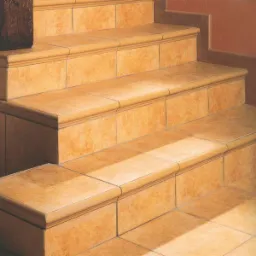 Wykończone schody z terakoty w ciepłych, beżowo-pomarańczowych odcieniach. Widoczne detale wykończenia krawędzi i fug. Dyskretne oświetlenie podkreśla fakturę materiału.