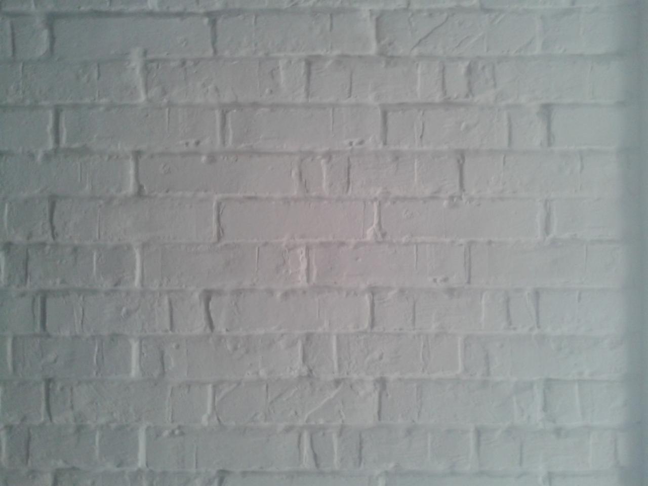 Biała ściana z cegieł, równomiernie oświetlona, z widoczną fakturą i spoinami. Minimalistyczny kadr skupiony na strukturze muru.