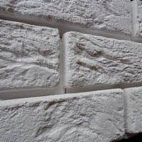 Białe, strukturalne płytki imitujące cegłę, ułożone w regularny wzór. Widoczne fugi i nieregularna faktura każdej płytki, z bliska, z delikatnym cieniem.