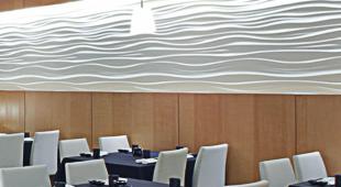 Nowoczesne oświetlenie LED w restauracji: falisty panel świetlny zamontowany na suficie, podkreślający drewniane ściany i eleganckie nakrycia stołów.