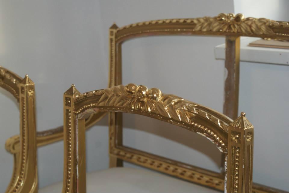 Fragmenty odrestaurowanych, złoconych krzeseł w stylu Ludwika XVI, z wyraźnymi detalami rzeźbionymi w drewnie. Widoczne ślady renowacji na jednym z elementów.