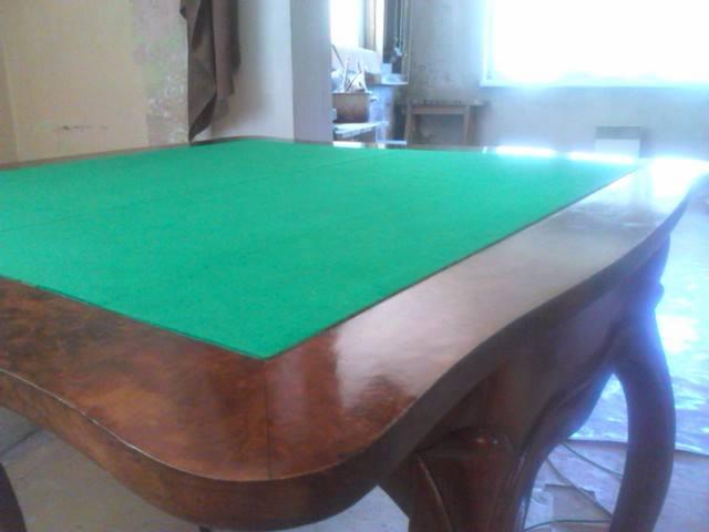 Odrestaurowany stół bilardowy z zielonym suknem i błyszczącym, ciemnym drewnem, widoczny w jasnym pomieszczeniu. Zakrzywione nogi stołu dodają mu elegancji.
