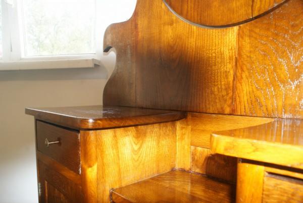 Błyszcząca, odnowiona toaletka z drewna w stylu art deco, z widocznym fragmentem okrągłego lustra i szufladą z metalowym uchwytem. Widoczna faktura drewna.