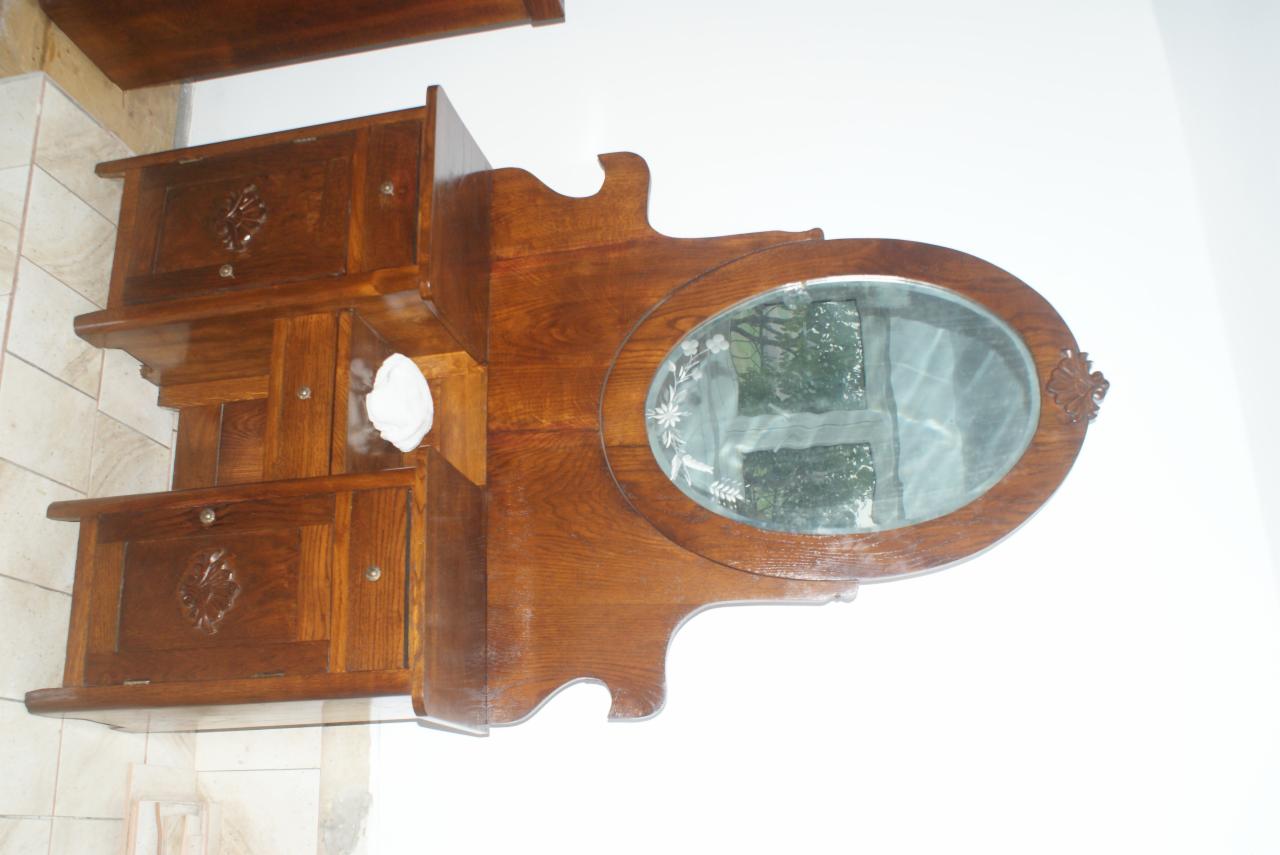 Antyczna, drewniana toaletka z owalnym lustrem zdobionym motywami roślinnymi i szafkami z rzeźbionymi frontami. Widoczne detale i wykończenie.
