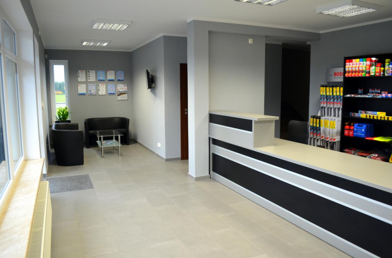 Wnętrze warsztatu samochodowego: recepcja z ladą, poczekalnia z sofą i stolikiem, ściana z certyfikatami, regał z akcesoriami samochodowymi marki Bosch.