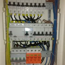 Rozdzielnica elektryczna z zainstalowanymi bezpiecznikami Legrand i zabezpieczeniami SIMTEC, widoczne kable w kolorach żółto-zielonym, niebieskim i brązowym, zamocowane w białej obudowie.