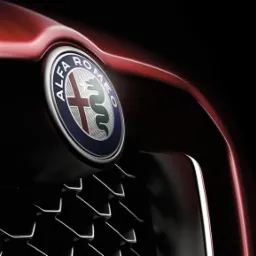 Szczegółowe ujęcie logo Alfa Romeo na czerwonym samochodzie z charakterystyczną kratką grilla.