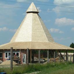 KERIM S.C. - Wodzierady: Nietypowa konstrukcja szkieletowa w budowie, przypominająca piramidę z drewnianym pokryciem, widoczny betoniarka i materiały budowlane.