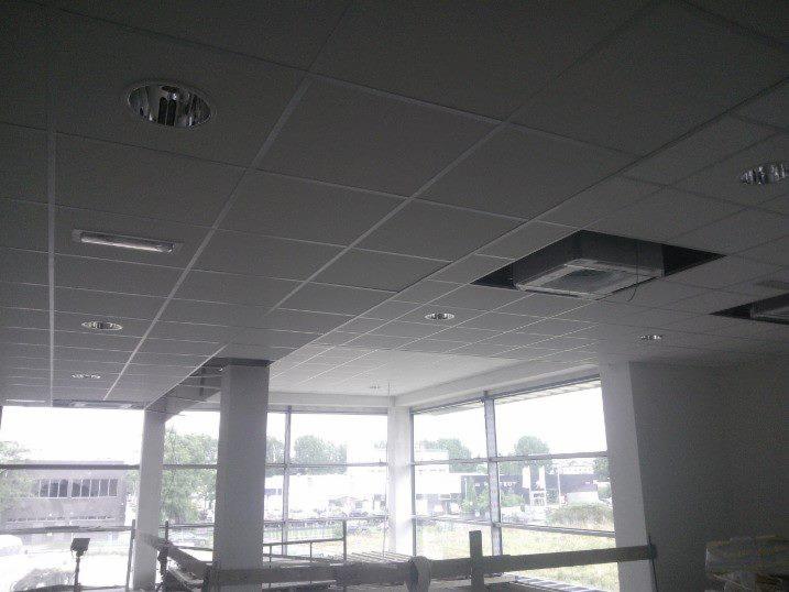 Sufit podwieszany z widoczną instalacją klimatyzacji i oświetleniem punktowym w jasnym pomieszczeniu z dużymi oknami, widok na zewnątrz.