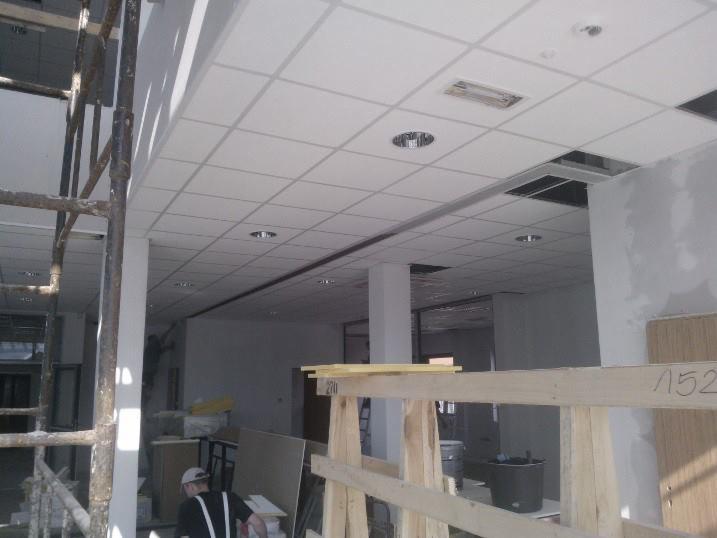 Sufit podwieszany w biurze podczas montażu, widoczne elementy konstrukcyjne, oświetlenie i rusztowanie. Ujęcie z budowy lub remontu.